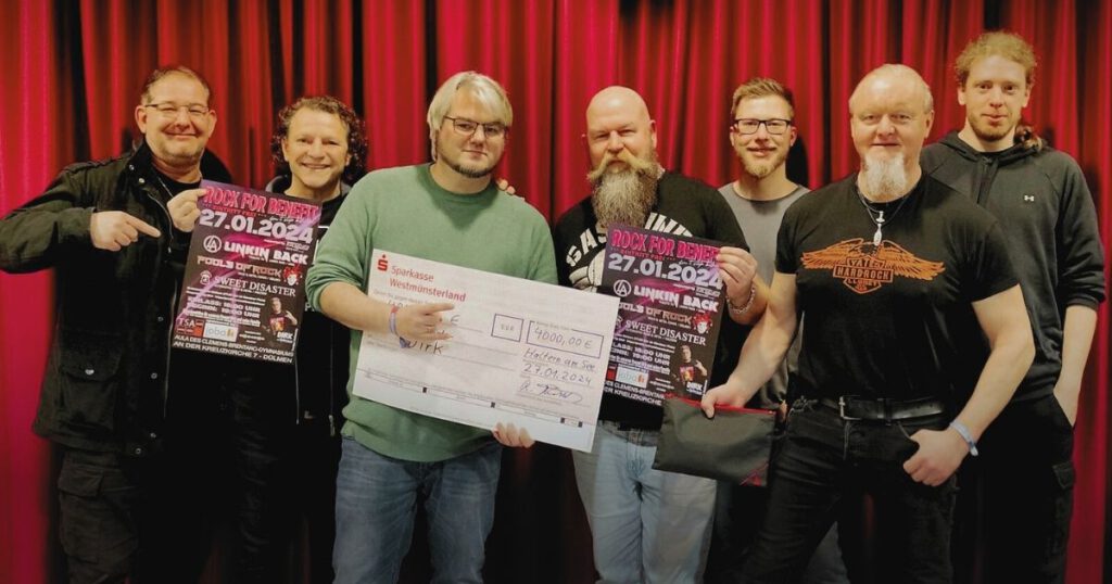 Gruppenfoto mit Scheck und Konzertplakaten vor rotem Vorhang.