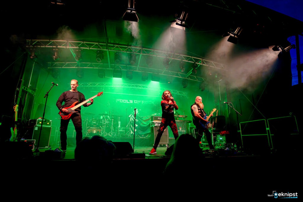 Rockband performt auf Bühne mit grünem Licht.