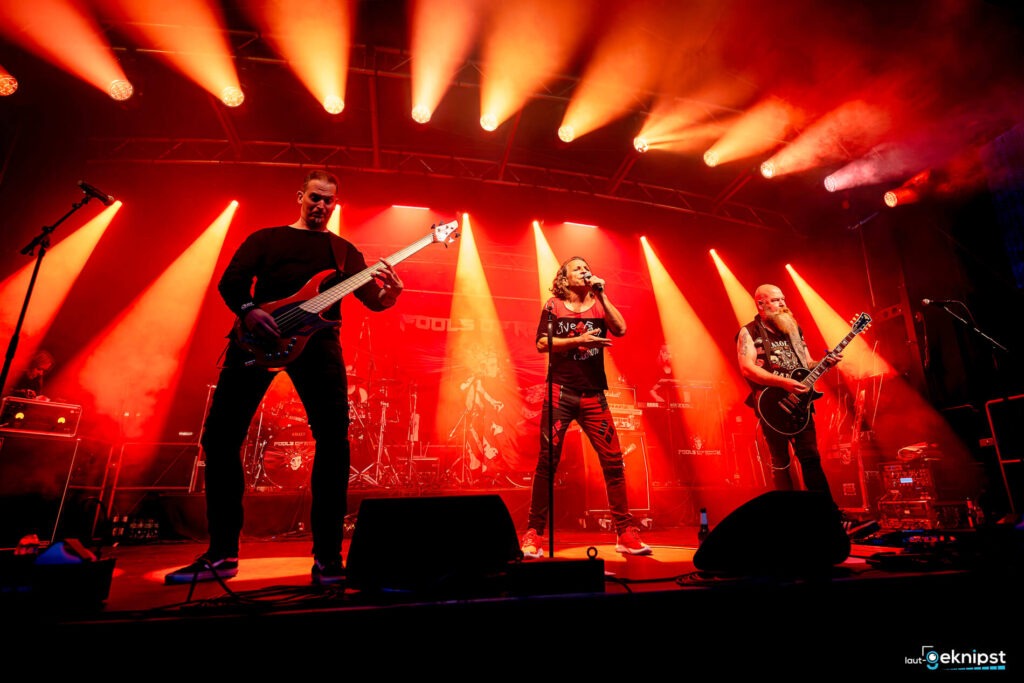 Rockband spielt live auf Bühne mit roten Lichtern.