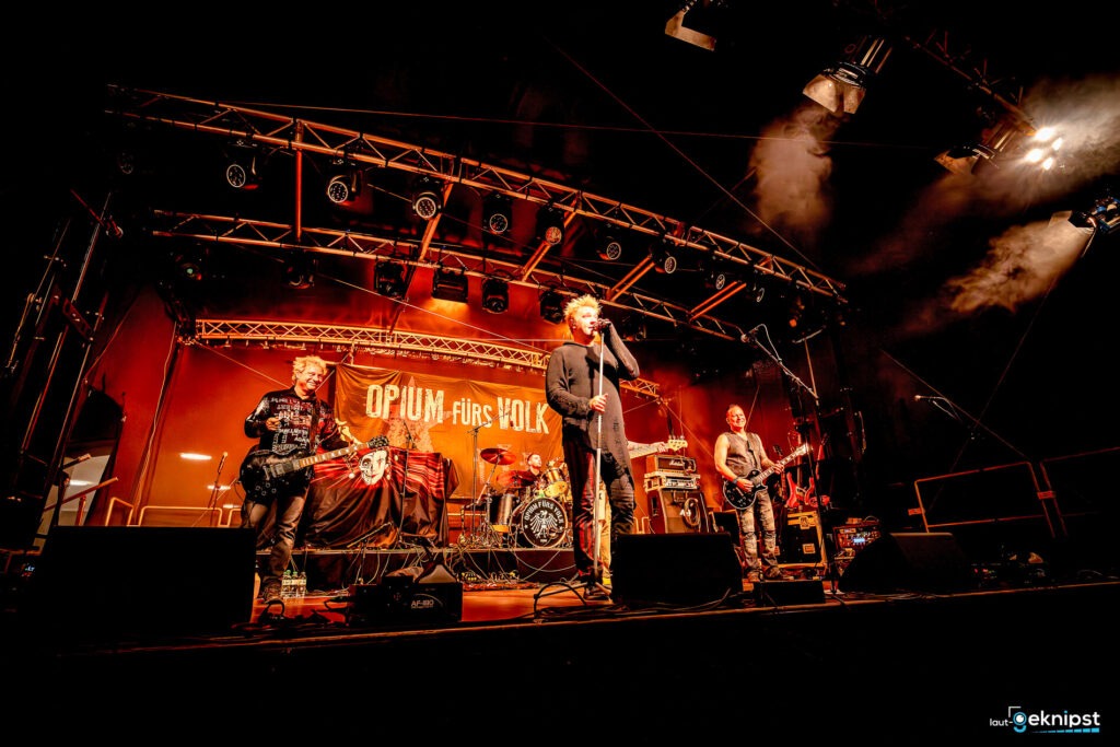 Band spielt Konzert auf Bühne mit Bannern.