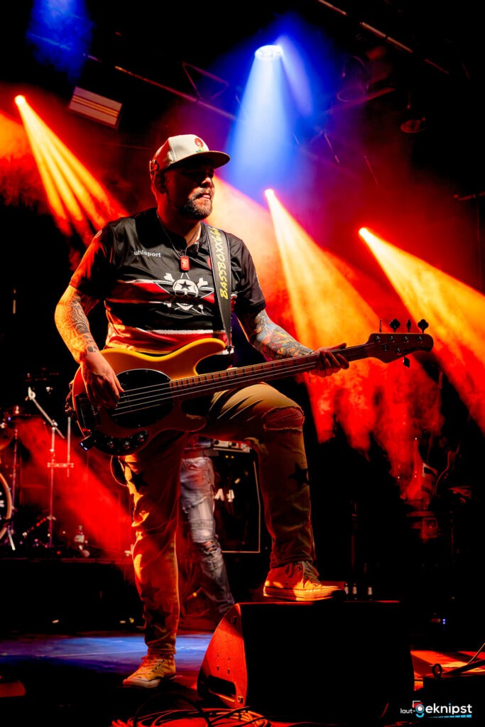 Bassist spielt Gitarre auf der Bühne unter bunten Lichtern.