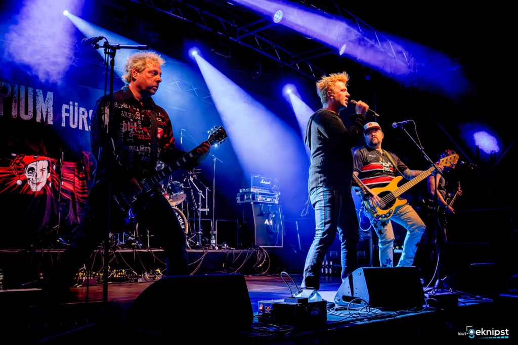 Band spielt Live-Konzert auf Bühne mit Lichteffekten.