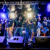Bandmitglieder auf Bühne mit Instrumenten und Lichtshow.