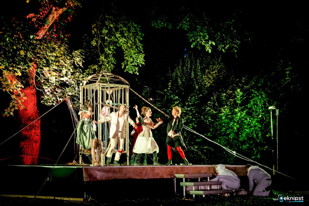 Theateraufführung im Freien mit bunt beleuchtetem Käfig