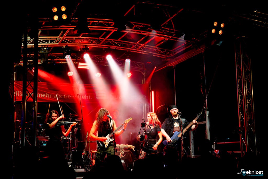 Band spielt live auf einer Bühne mit rotem Licht.