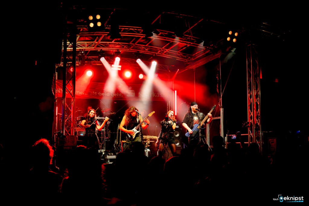 Band spielt Live-Konzert auf roter Bühne.