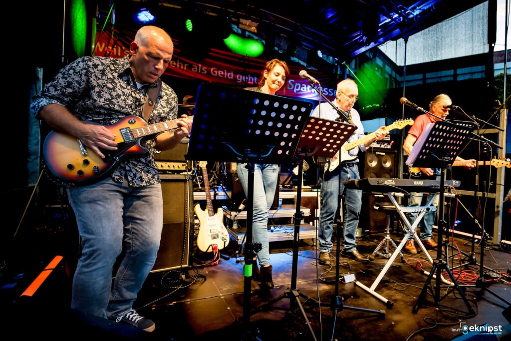 Band spielt auf einer Bühne Gitarre und Keyboard.