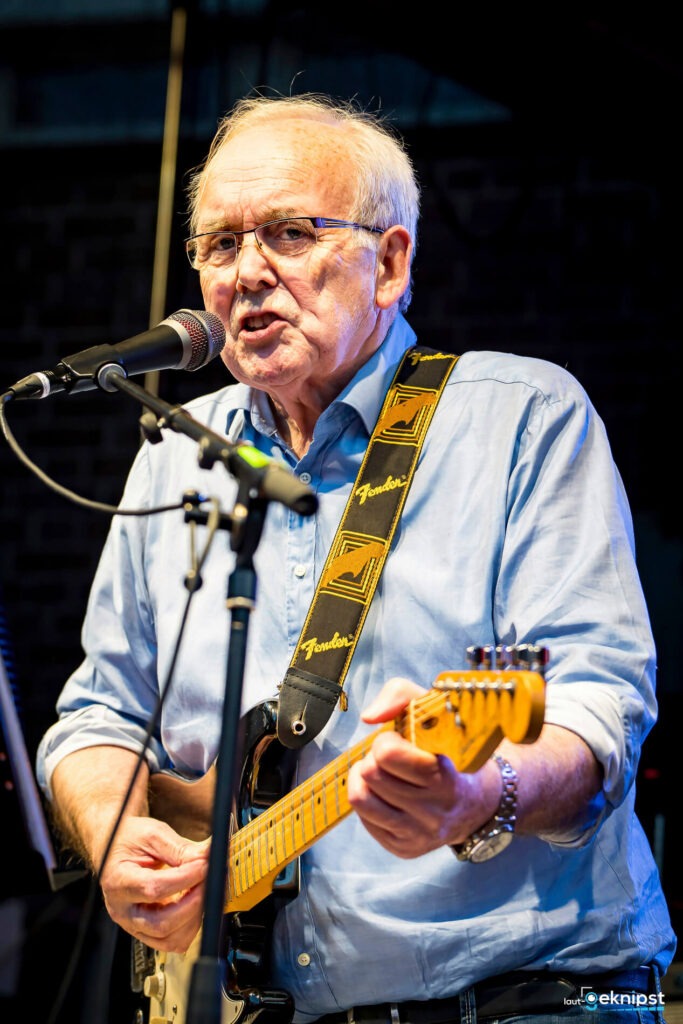 Älterer Mann spielt Gitarre auf der Bühne.