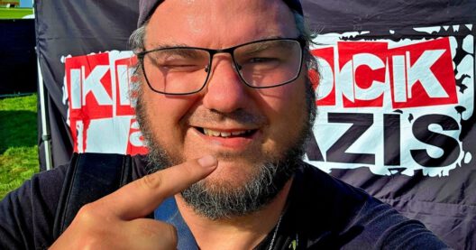 Person vor Plakat macht Selfie mit Fingerzeig.