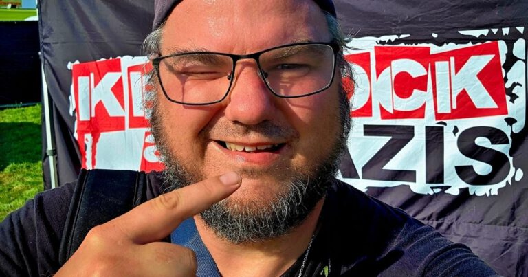 Person vor Plakat macht Selfie mit Fingerzeig.
