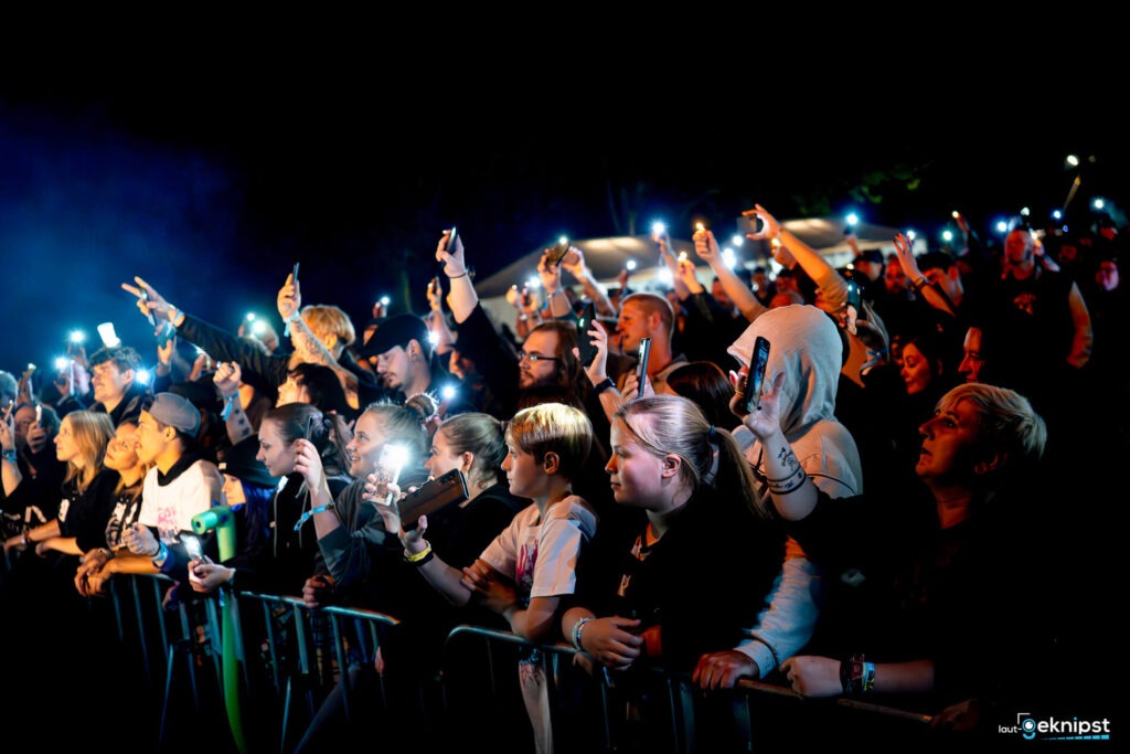 Menschenmenge bei Konzert, Handys leuchten in der Dunkelheit.