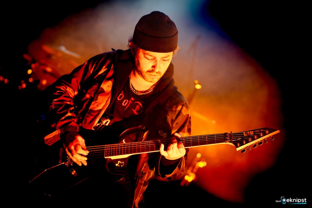 Mann spielt E-Gitarre vor orangefarbenem Hintergrund.