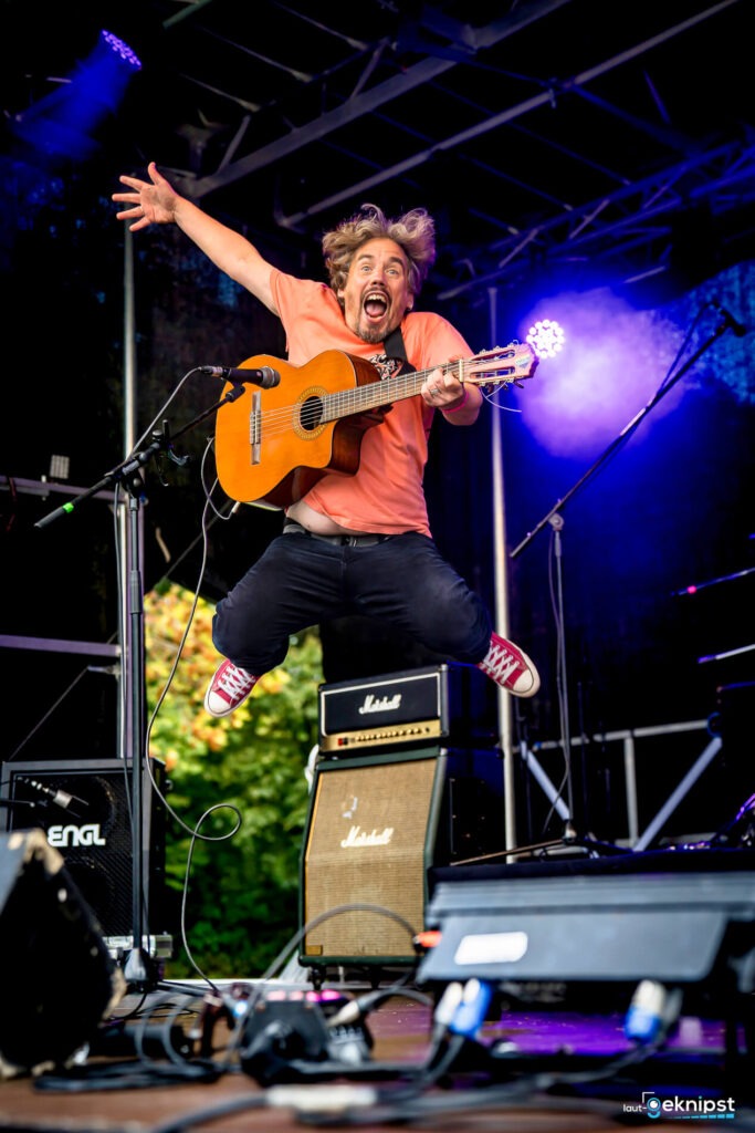 Springender Musiker mit Gitarre auf Bühne