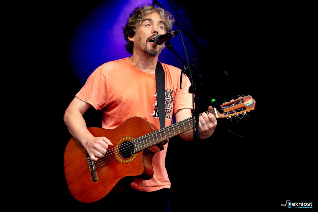 Musiker spielt Gitarre und singt auf Bühne.
