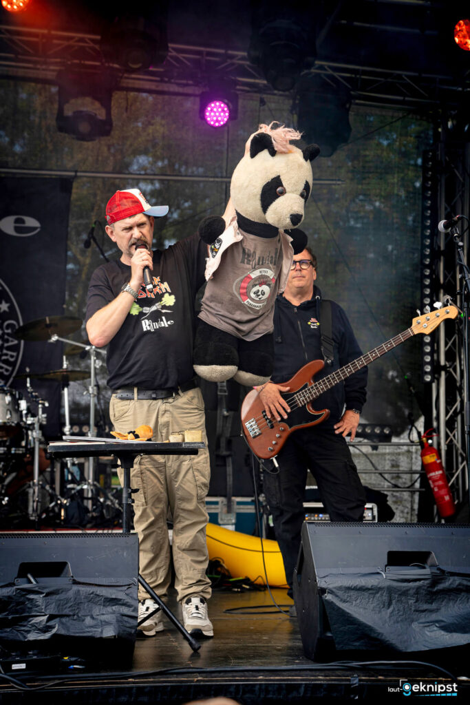 Mann mit Plüschtier auf Bühne singt.