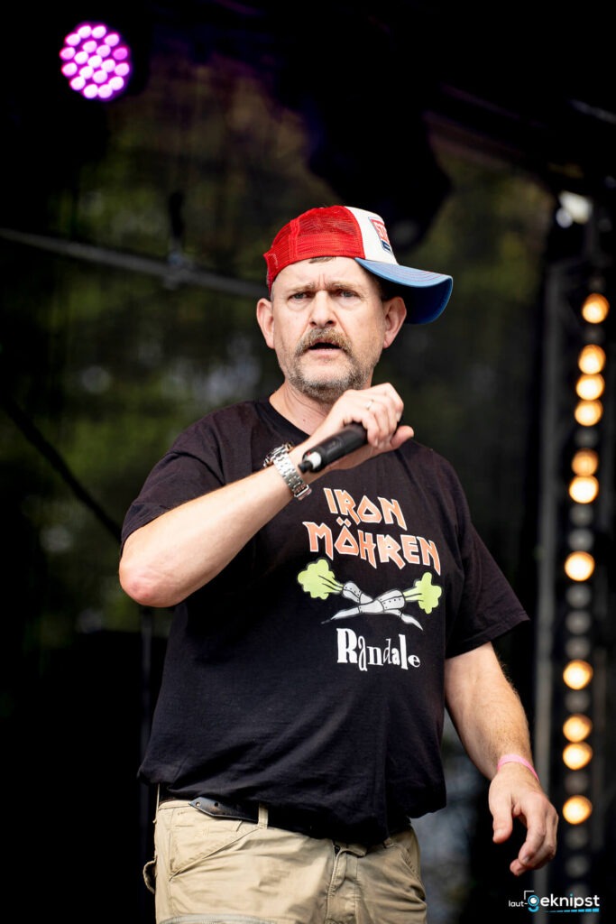 Mann mit Mikrofon und bunter Kappe auf der Bühne.