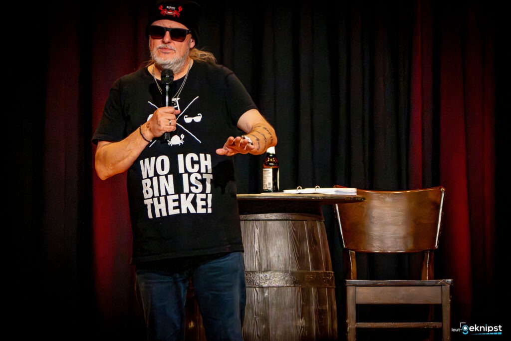 Person auf Bühne mit Mikrofon und T-Shirt-Slogan.