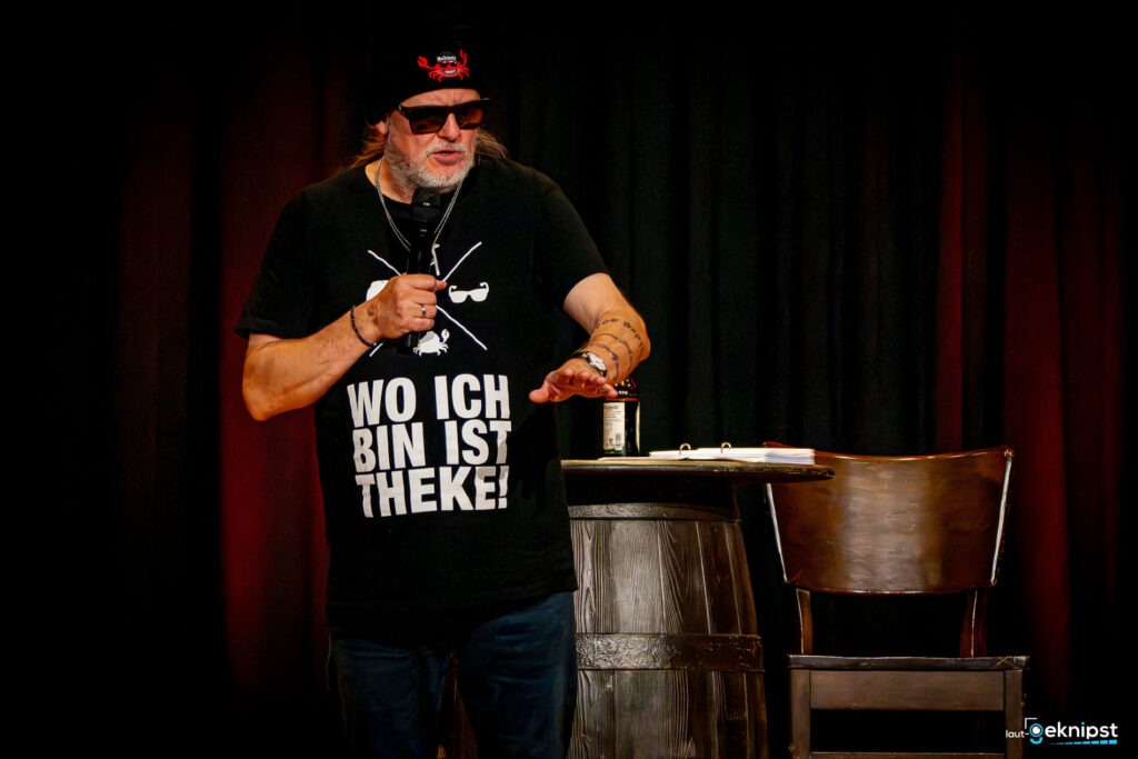 Mann mit T-Shirt auf Bühne hält Mikrofon