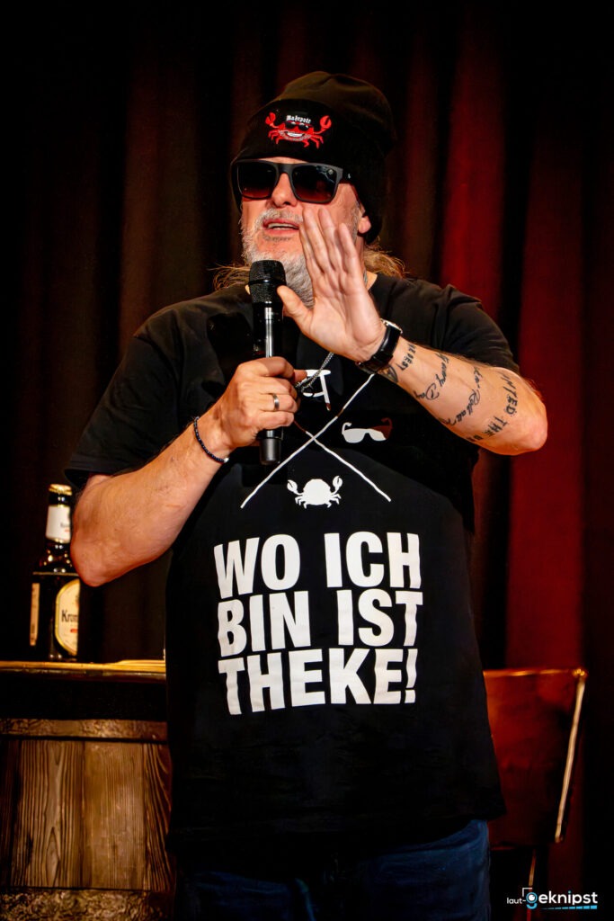 Mann trägt T-Shirt mit Theken-Slogan und Mikrofon