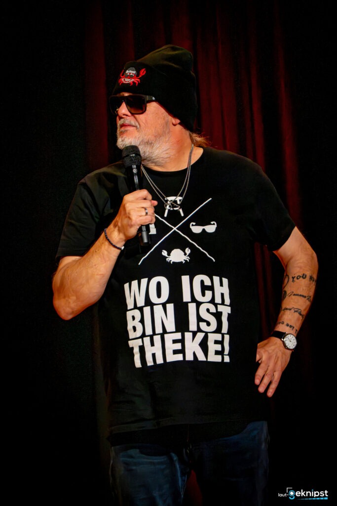 Person auf der Bühne mit schwarzem T-Shirt und Mütze.
