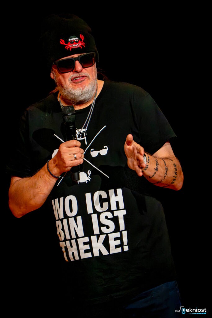 Person mit Mütze und Mikrofon, schwarzes T-Shirt.