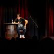 Markus Krebs auf Bühne sitzt an Tisch mit Mikrofon.