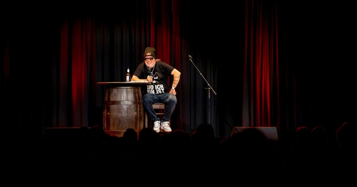 Markus Krebs auf Bühne sitzt an Tisch mit Mikrofon.
