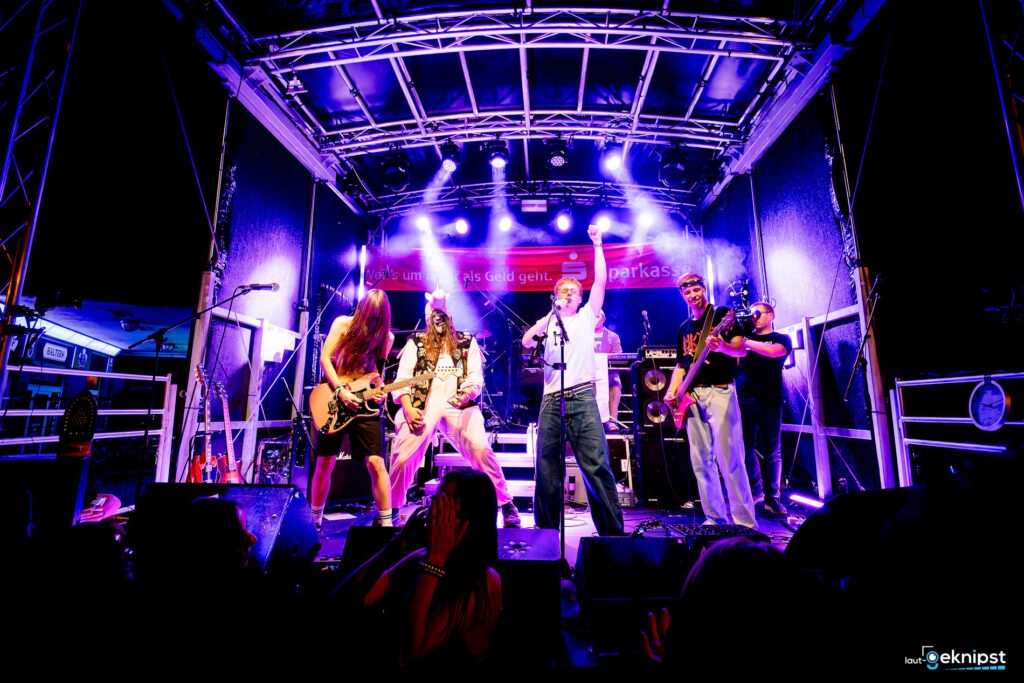 Band spielt Live-Musik auf Bühne mit Lichteffekten.