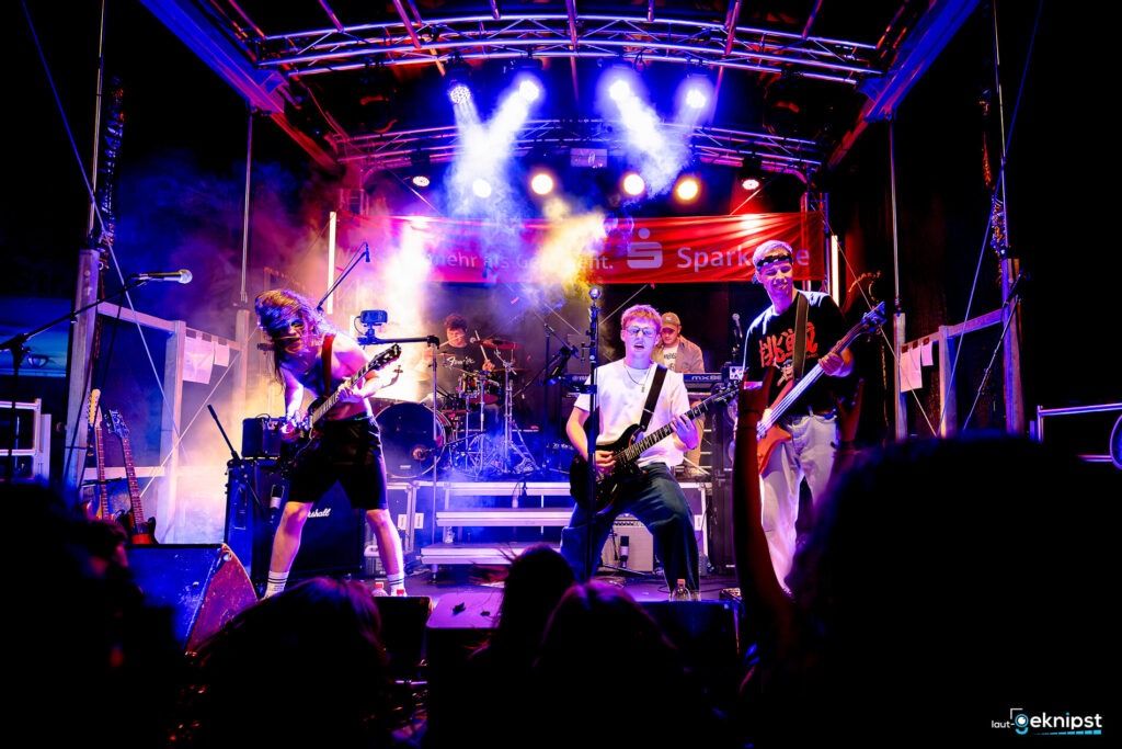 Live-Band auf einer beleuchteten Bühne spielt Musik.