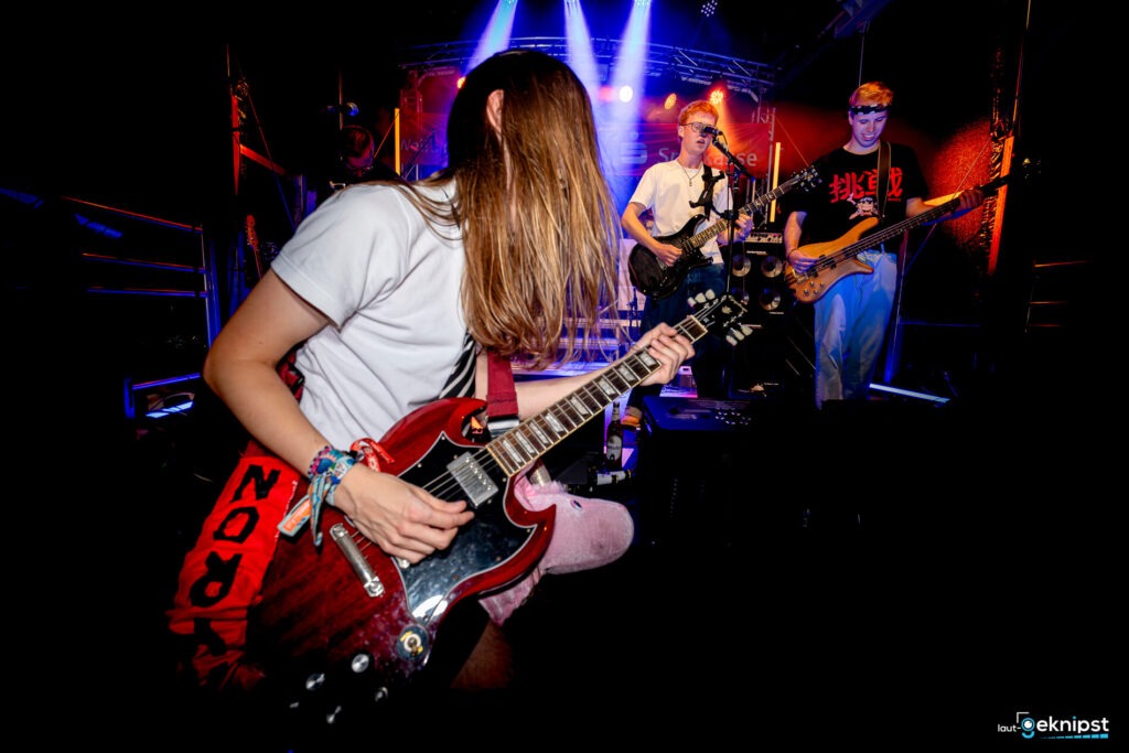 Rockband spielt auf Bühne, Gitarrist im Vordergrund.