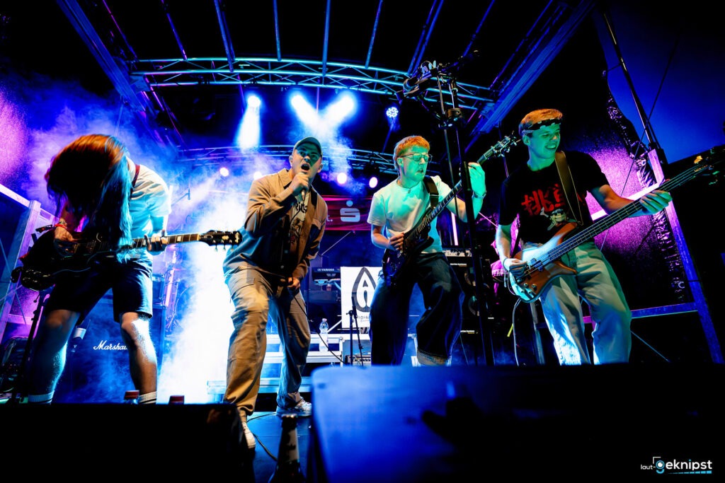 Rockband auf Bühne mit Lichteffekten.