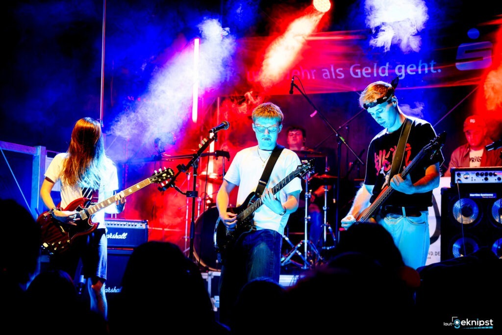 Band spielt auf beleuchteter Bühne mit Gitarren.