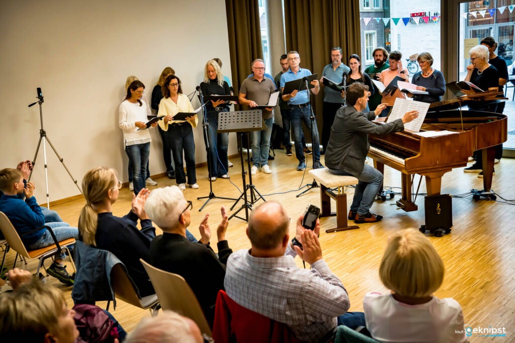 Chor singt neben Klavier, Publikum applaudiert.