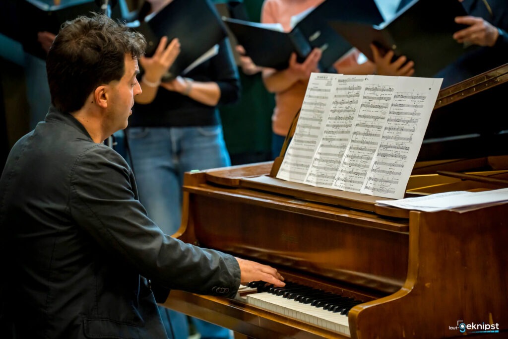 Mann spielt Klavier mit Chor im Hintergrund
