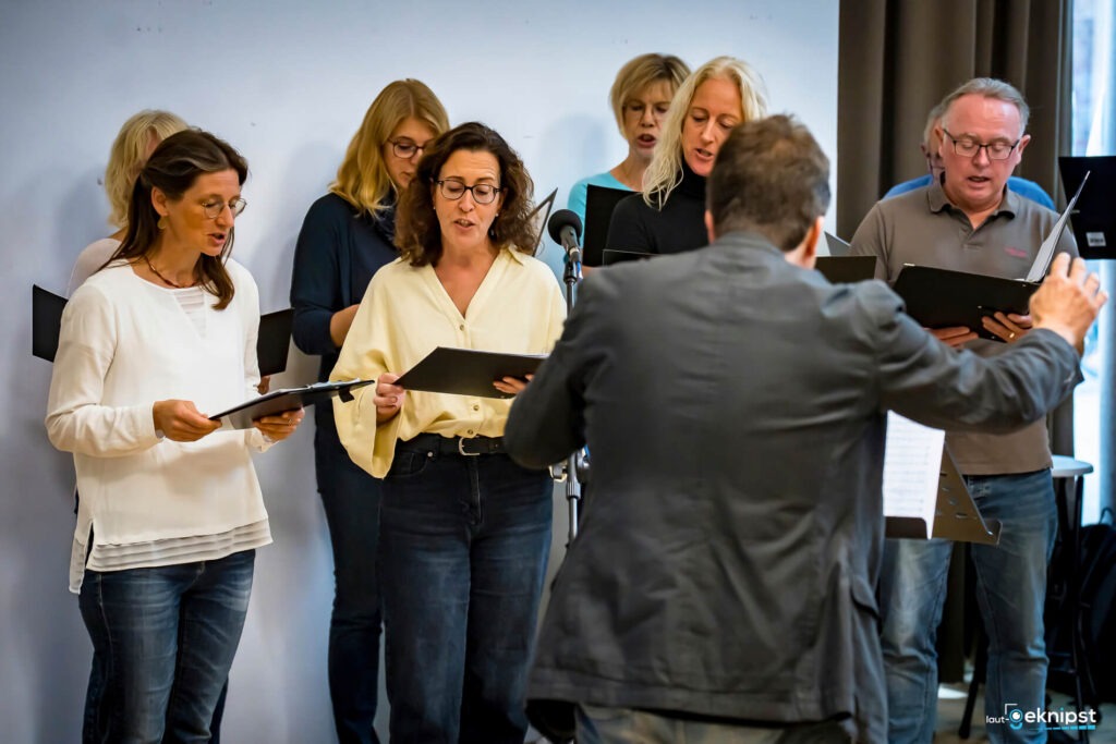 Chor singt mit Dirigent vor Publikum.