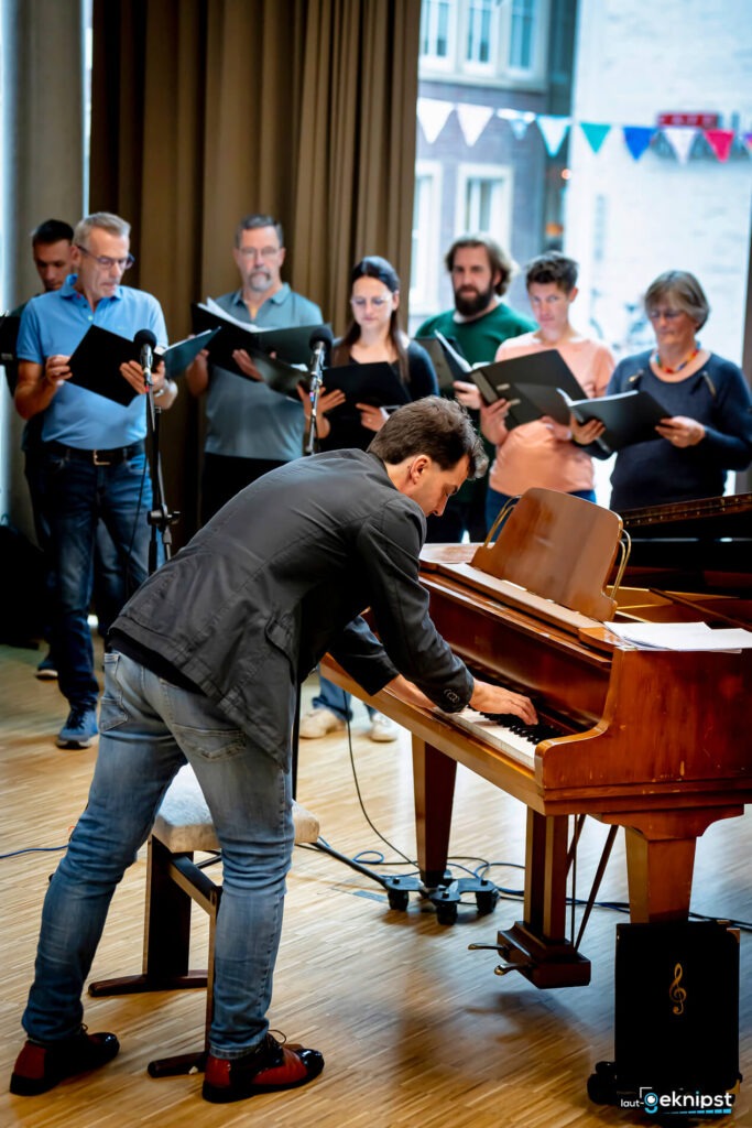Pianist spielt vor singendem Chor in einem Raum.