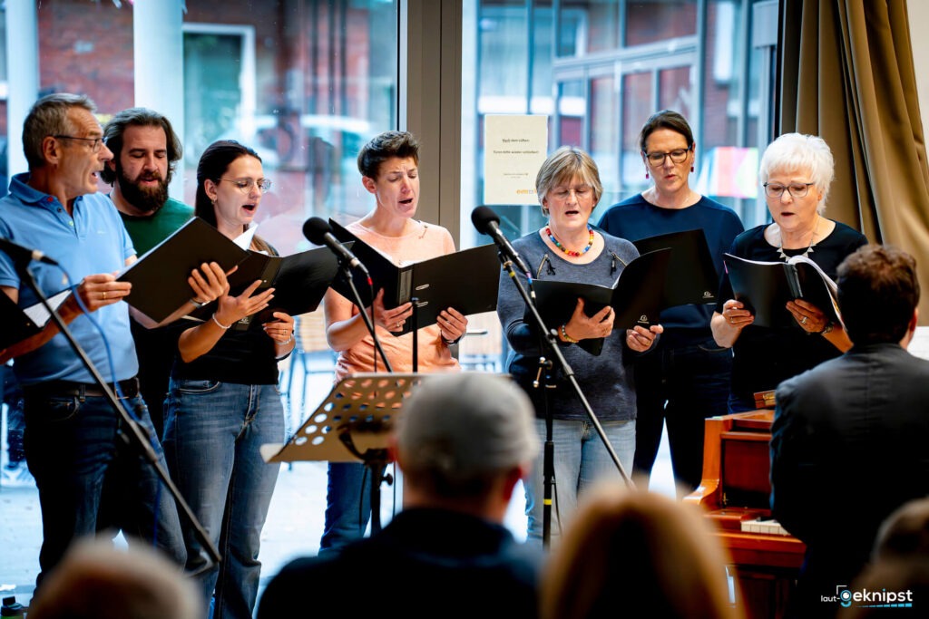 Chor singt vor Publikum mit Noten in Händen.