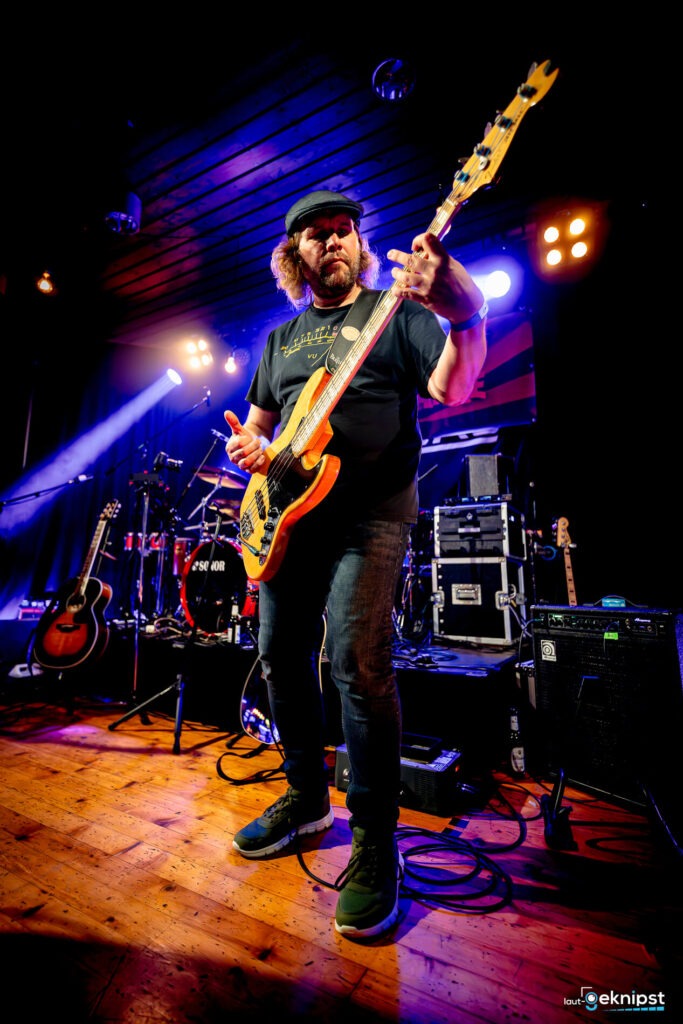 Musiker spielt Bass auf Bühne, bunte Lichter.