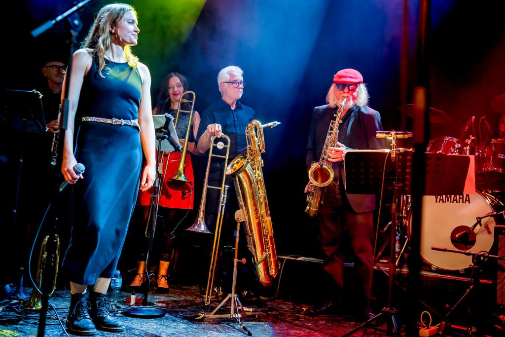 Bluesband auf der Bühne mit Sängerin und Blasinstrumenten.