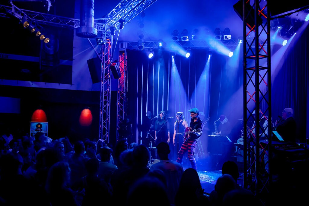 Konzert mit Bühne und Band in blauem Licht.
