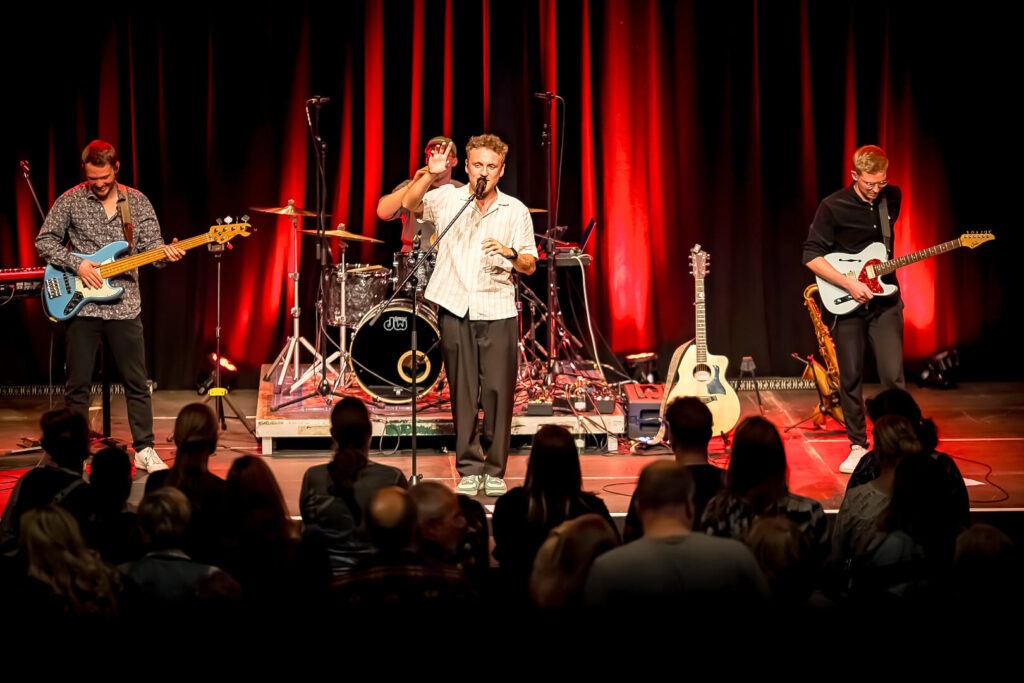 Band spielt Konzert auf Bühne mit rotem Licht.