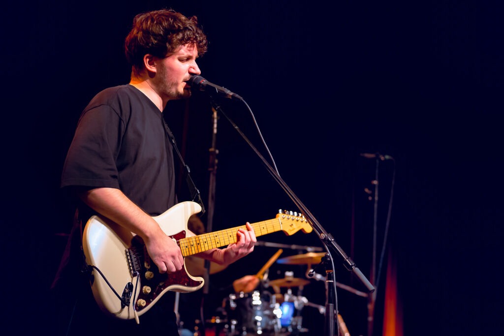 Musiker spielt Gitarre und singt auf Bühne.