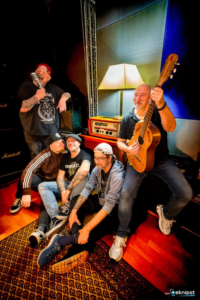 Bandmitglieder mit Instrumenten lächeln in Tonstudio.