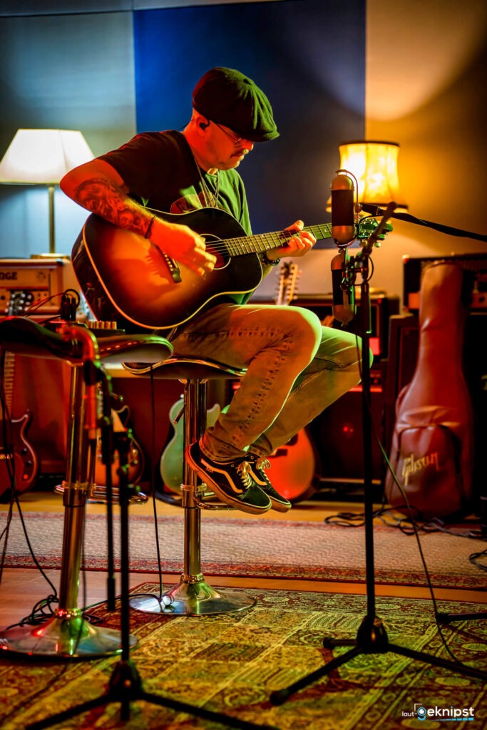Mann spielt Gitarre im Musikstudio mit Mikrofon