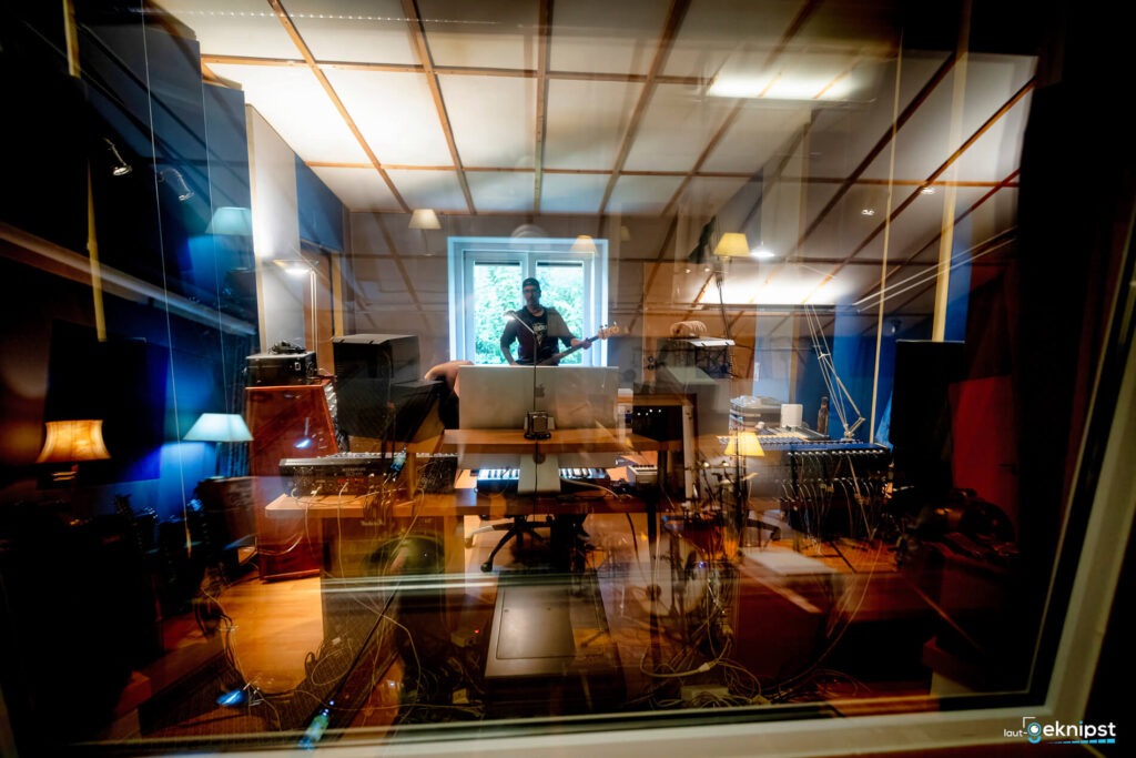 Musikstudio mit Musikern und Instrumenten hinter Glasfenster.