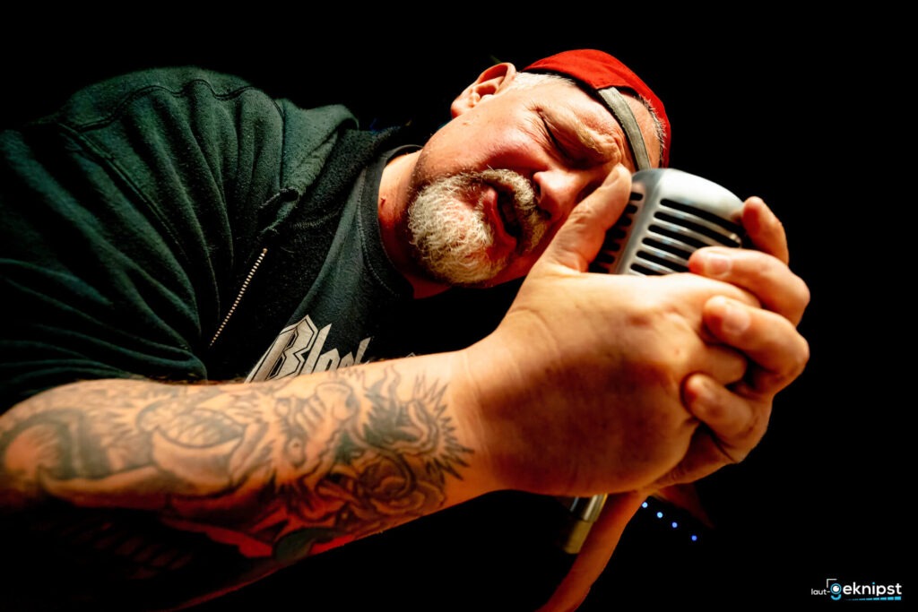 Mann singt in Retro-Mikrofon mit Tattoo am Arm.