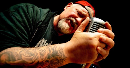 Mann singt in ein Mikrofon mit Tattoo.