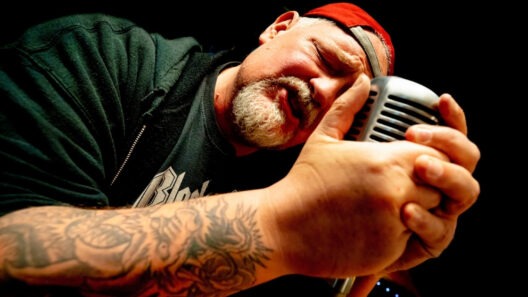 Mann singt in ein Mikrofon mit Tattoo.