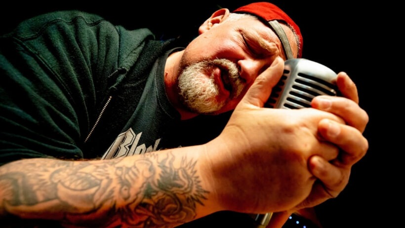 Mann singt in ein Mikrofon mit Tattoo.
