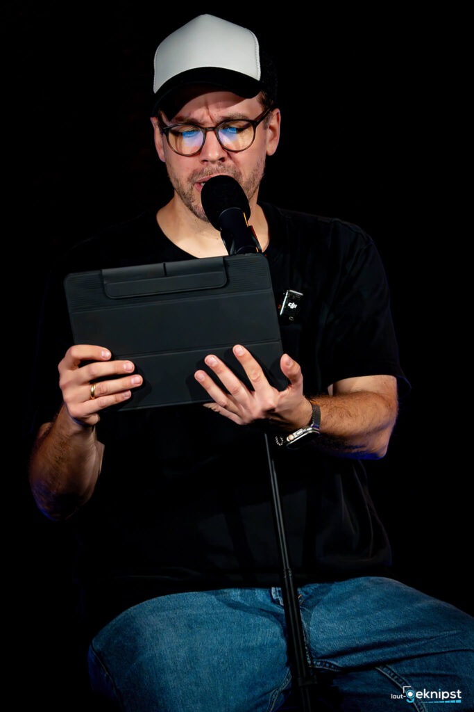 Mann liest auf Bühne von einem Tablet vor.